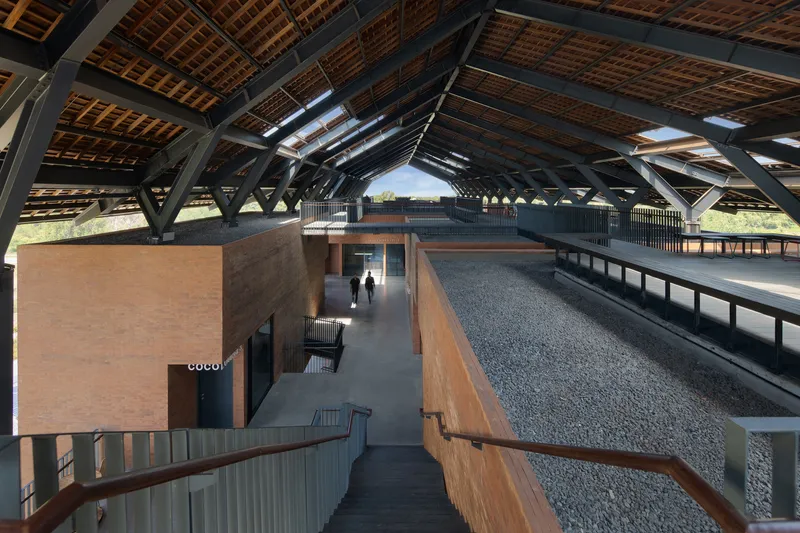 Elevated walkway view of the central courtyard beneath a vaulted steel and timber roof with skylights