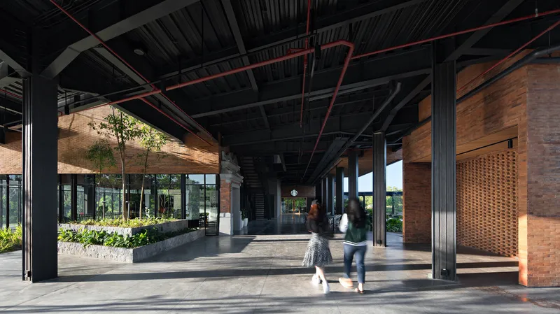 Covered walkway with black steel columns and exposed ceiling structure as two visitors walk through afternoon light