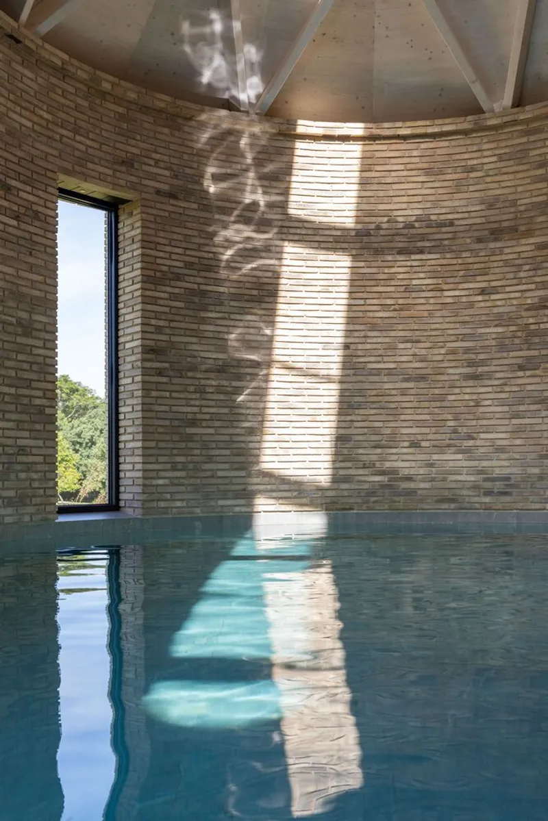 Interior pool beneath a curved brick wall with narrow window and dappled sunlight patterns