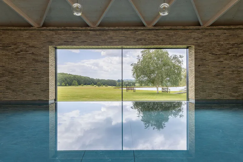 Indoor pool with floor-to-ceiling glazing reflecting clouds and green lawn beyond
