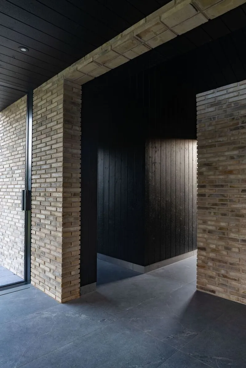 Entry passage with yellow brick walls and black timber-clad alcove