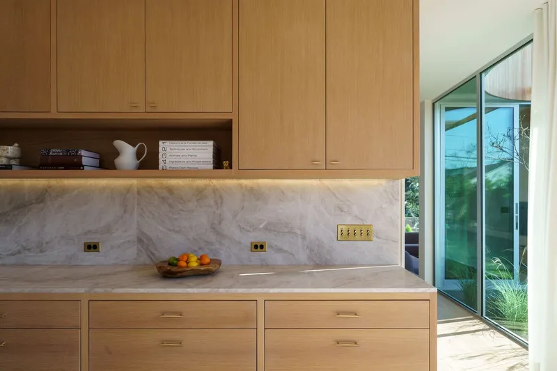 Kitchen cabinetry with marble backsplash and brass electrical outlets beside sliding glass door