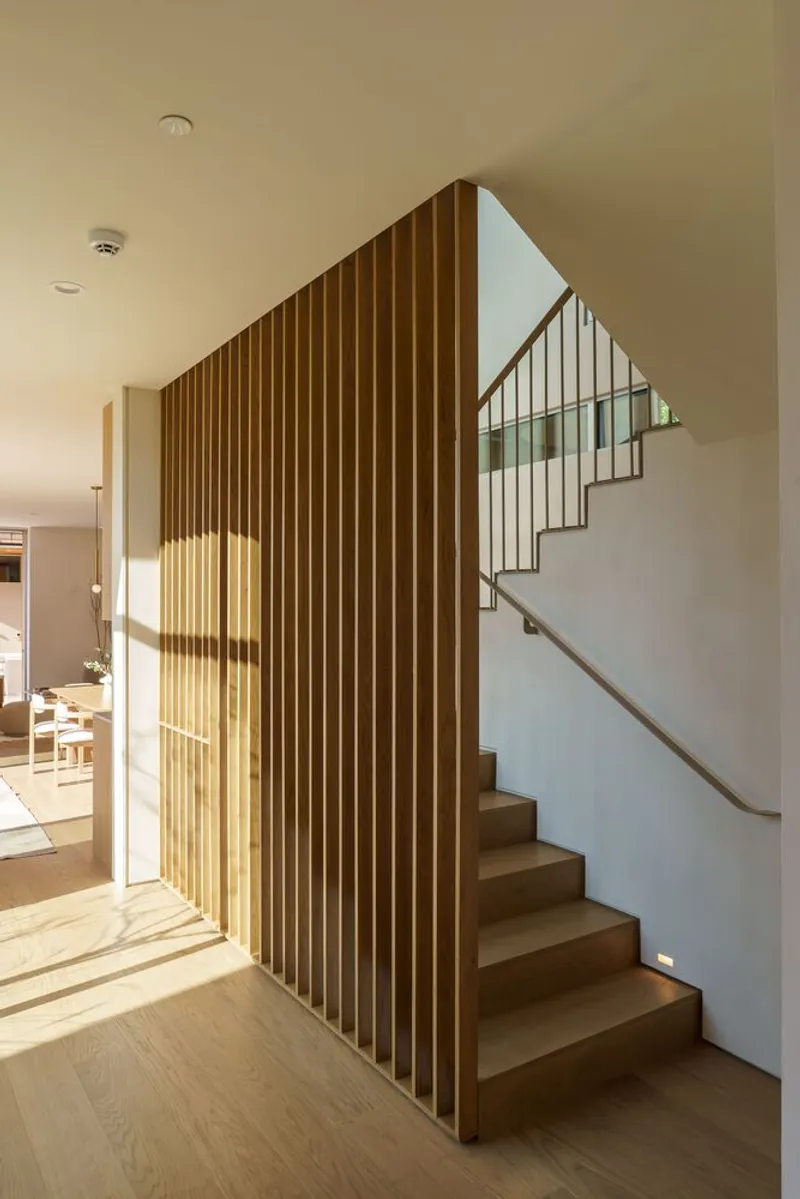 Interior staircase with vertical timber slat screen and white wall with sunlight streaming through