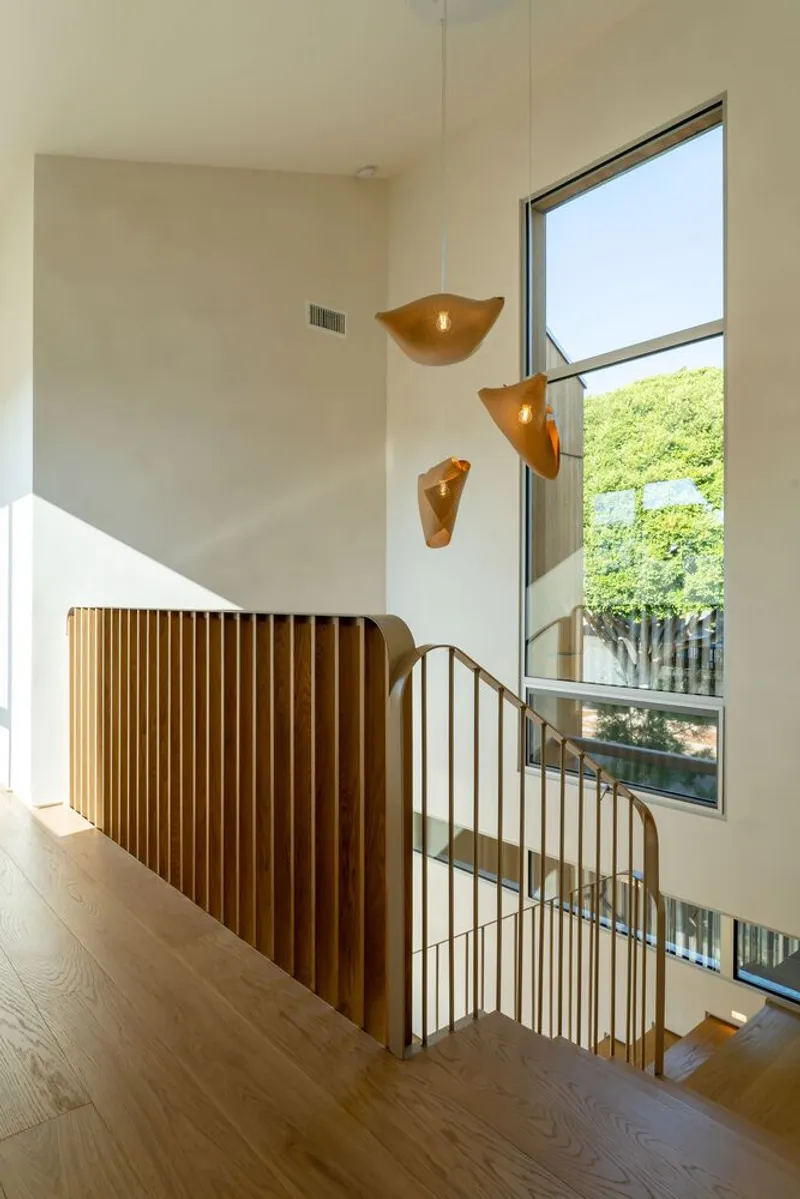 Two-story stairwell with curved timber slat screen and tall window framing summer foliage outside