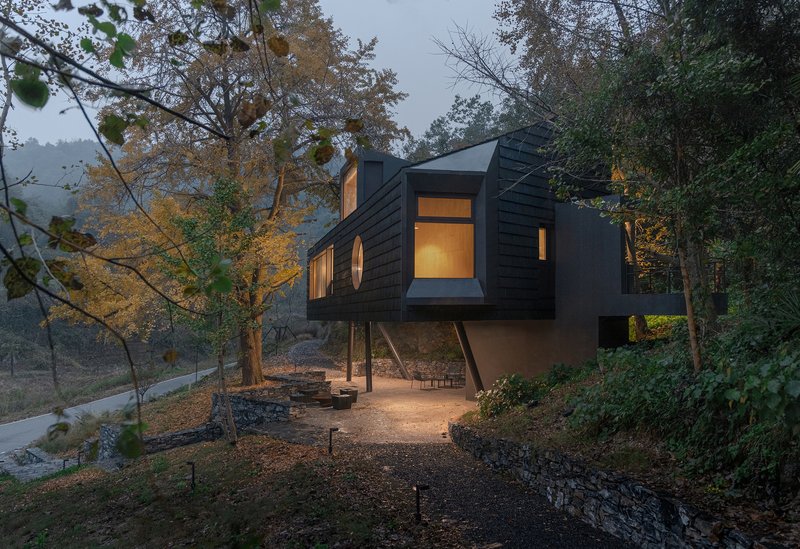 Elevated structure on steel columns with illuminated windows glowing at dusk among sparse trees