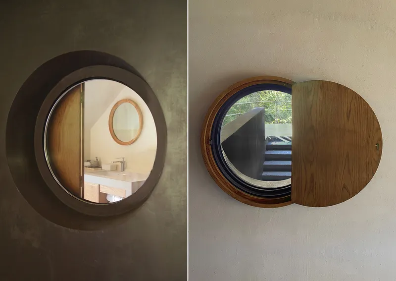 Two circular windows with timber shutters framing interior views of bathroom sink and staircase