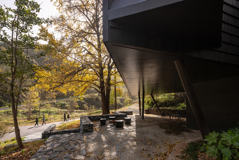 Covered seating area beneath the cantilevered structure with stone pavers and dappled afternoon light