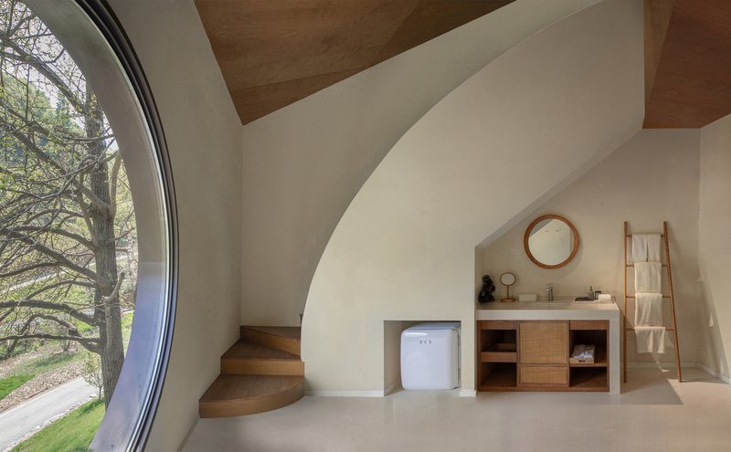 Bathroom with curved plaster stair, timber vanity unit, and floor-to-ceiling curved glass overlooking bare trees