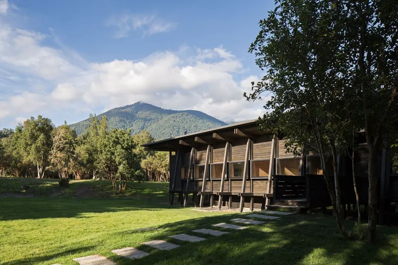 Timber facade with diagonal bracing columns set on a grassy clearing beneath a distant mountain