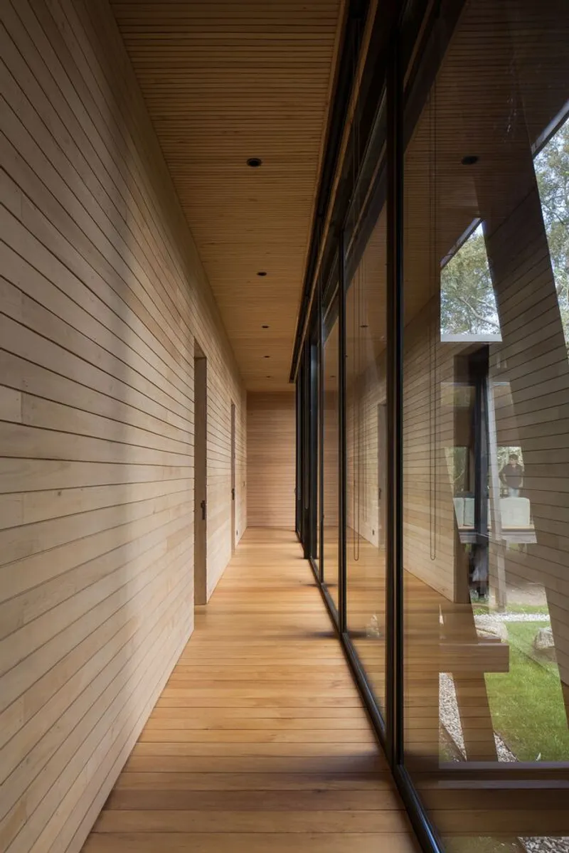 Wood-lined corridor with full-height glazing running along one side overlooking the landscape