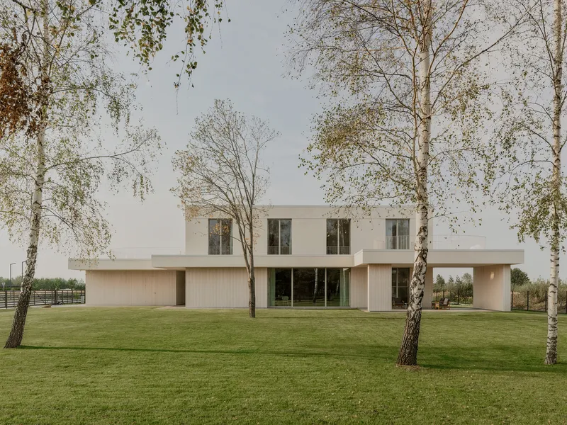 Rear facade with vertical ribbed timber base and white upper volume viewed across a lawn with birch trees
