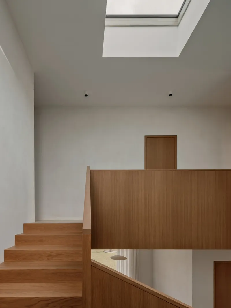 Split-level timber stair landing with skylight above and white walls enclosing the circulation space