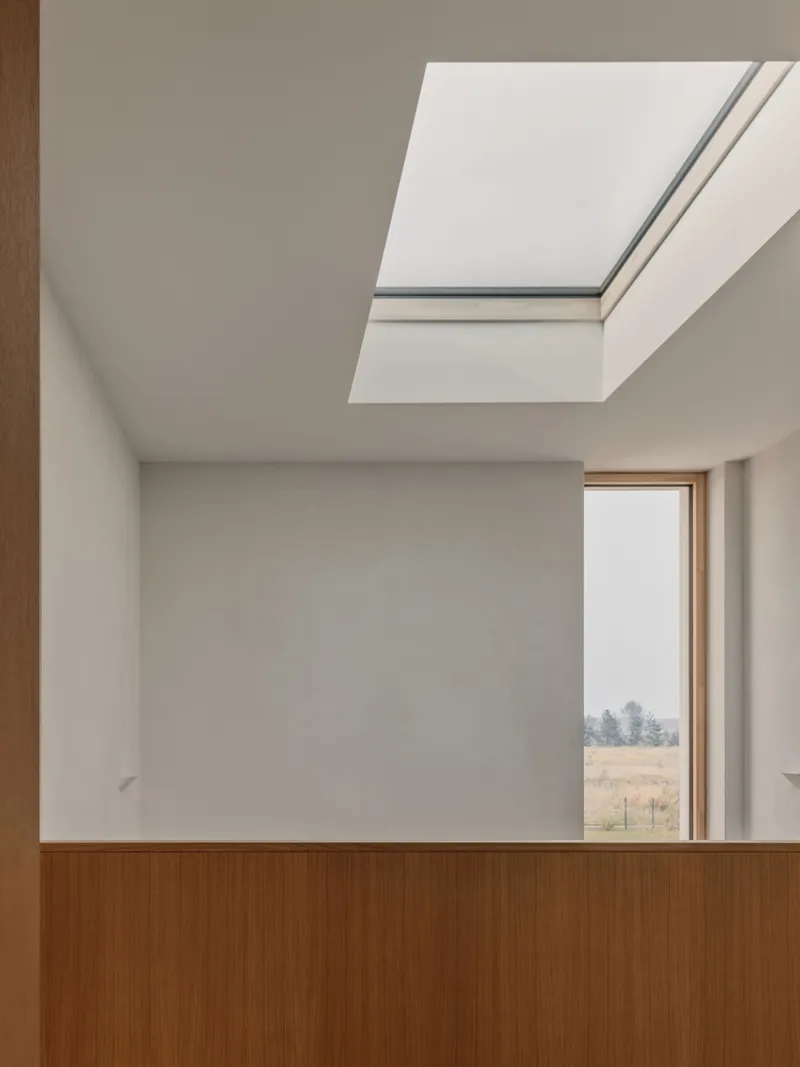 Upper hallway corner with timber balustrade, skylight overhead, and framed view of distant field landscape