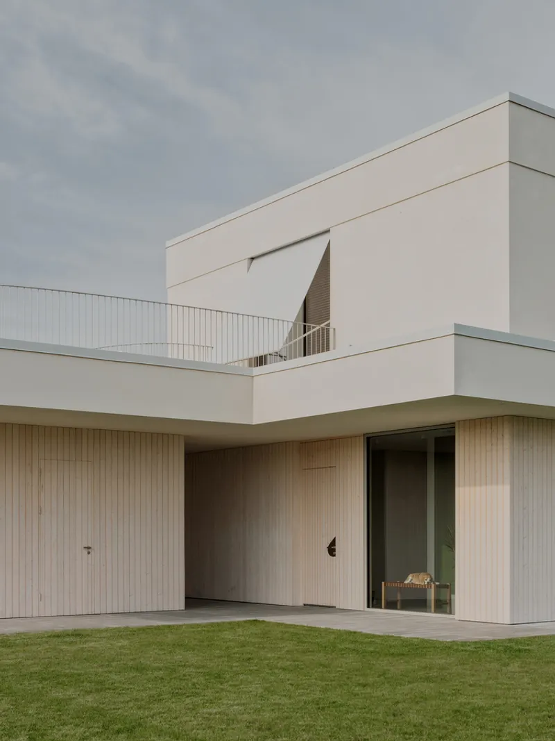 Ground floor facade with vertical timber cladding and white stucco volumes under an overcast sky