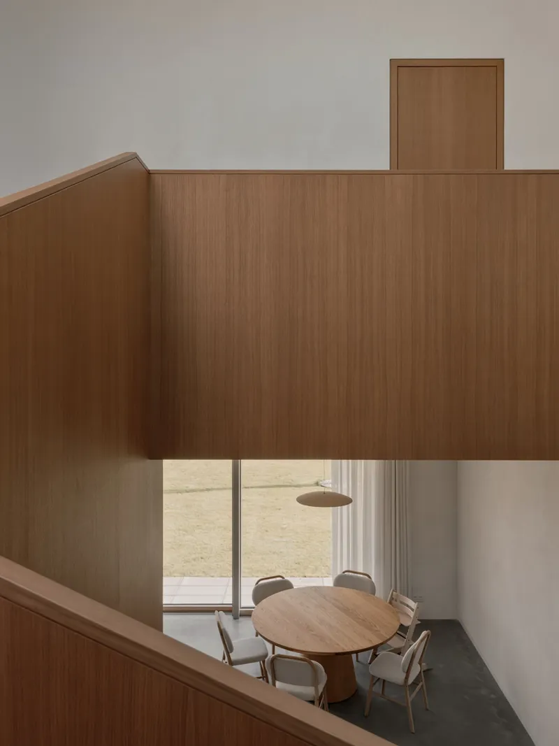 View from upper balcony into double-height dining space with timber box and circular table below
