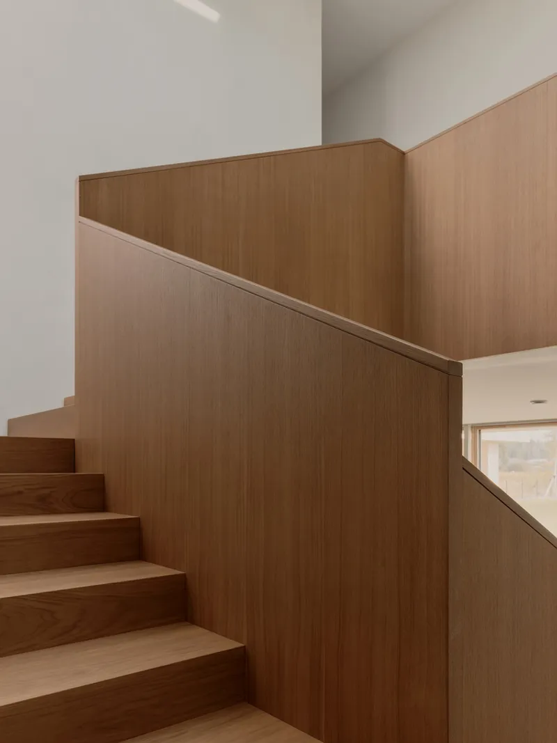 Timber staircase with tall wood-paneled walls rising through a white plaster volume