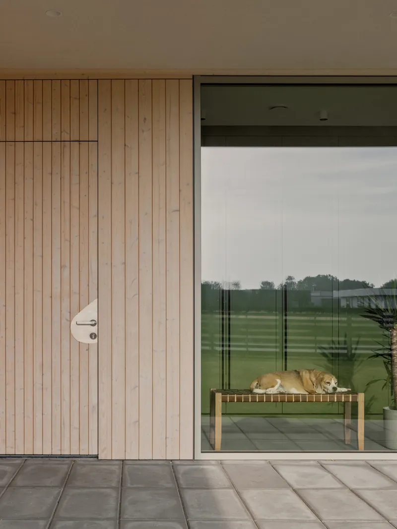 Covered terrace with vertical timber cladding and recessed door beside floor-to-ceiling glass overlooking lawn