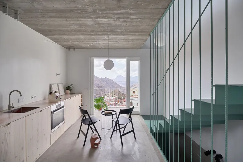 Kitchen with pale wood cabinets and green steel balustrade beside a window framing distant mountains