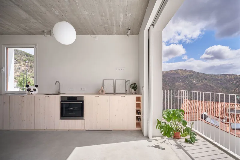Kitchen opening to a metal railing balcony with potted plant and mountainous terrain beyond