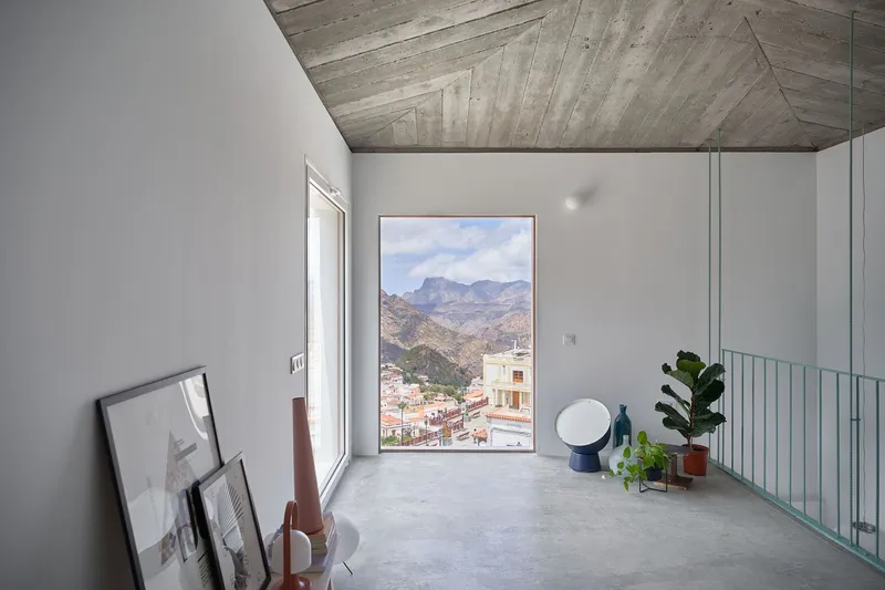 Tall window framing a mountain village view beside a green steel railing and polished concrete floor
