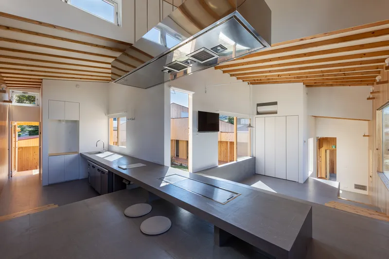 Open kitchen with steel island, stainless hood, and exposed timber ceiling beams under bright daylight