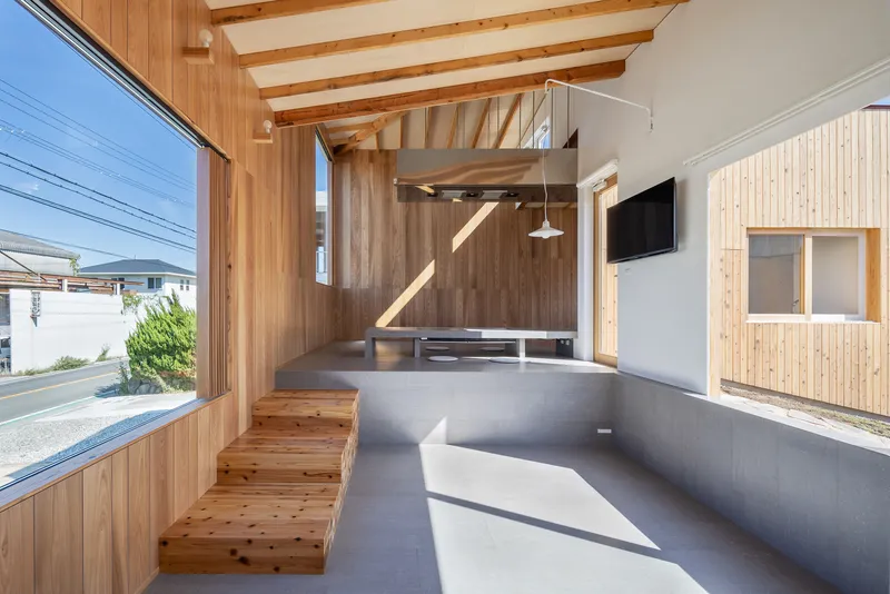 Living area with built-in timber bench seating, concrete floor, and exposed rafters framing exterior views