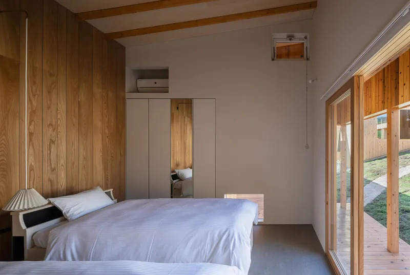 Bedroom interior with timber wall paneling, exposed ceiling beams, and glazed sliding doors overlooking the courtyard