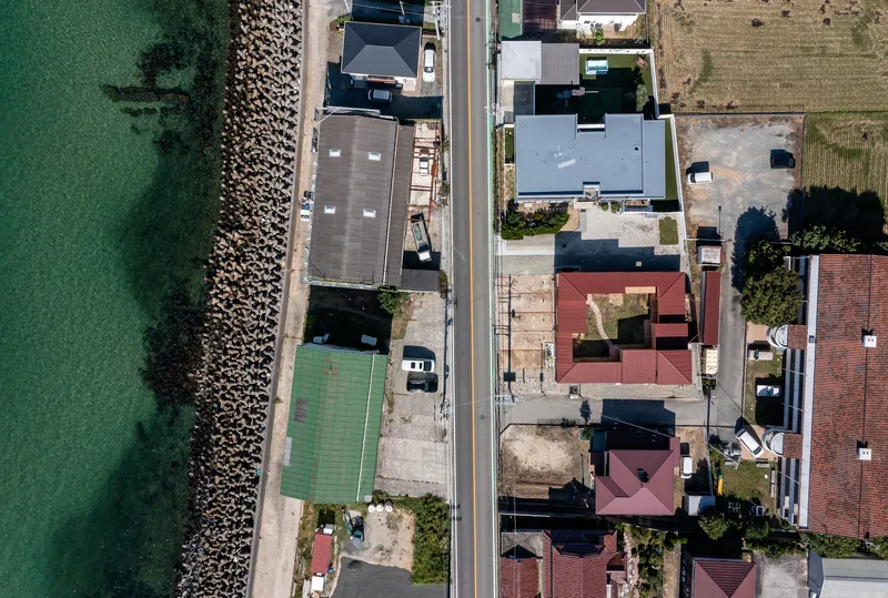 Drone view of the compound's maroon roofs and courtyard configuration along a coastal road