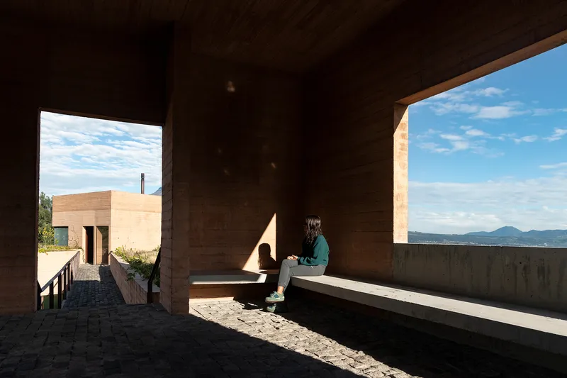 Covered terrace with rammed earth walls framing two openings to the landscape and distant mountains