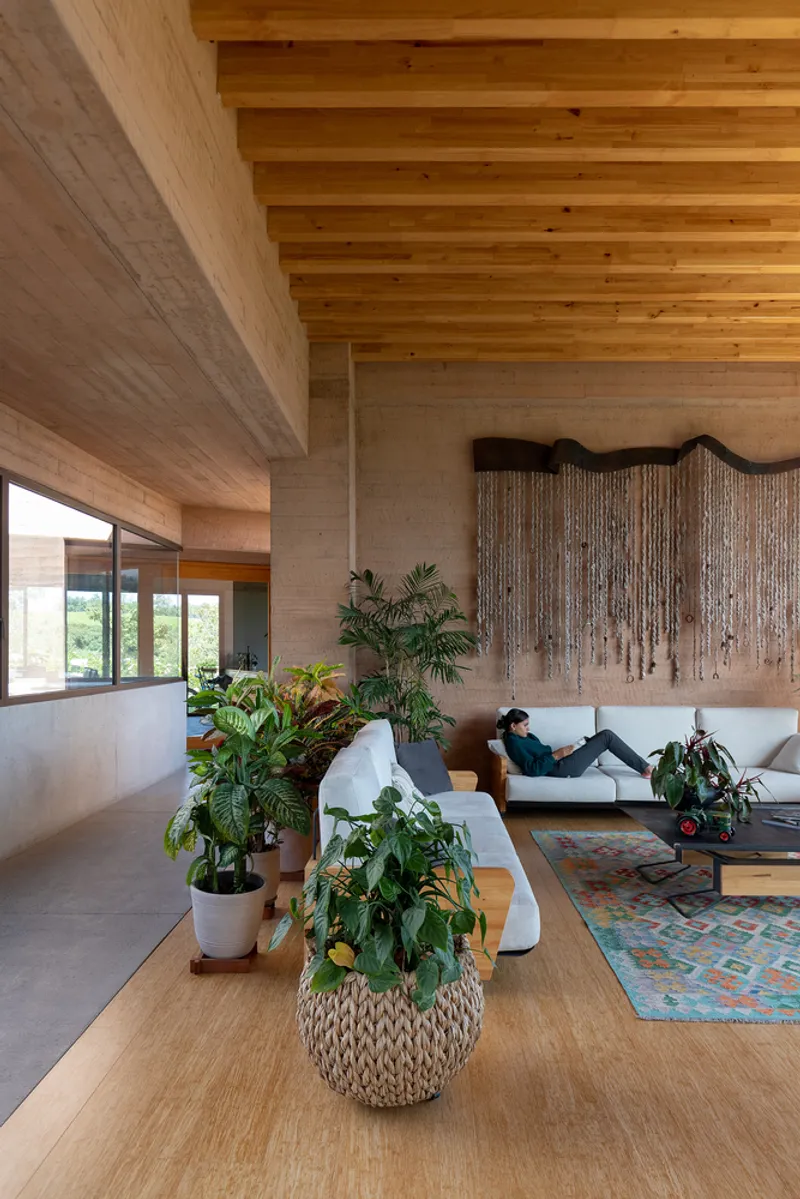 Double-height living space with exposed timber ceiling beams and rammed earth walls with potted plants