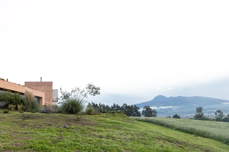 Rammed earth structure anchored on a sloping lawn with valley and peaks beyond