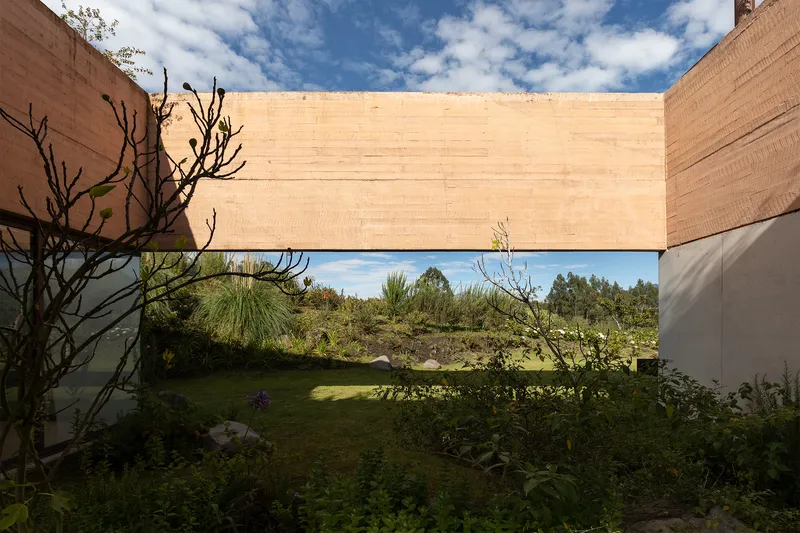 Timber-clad bridge spanning between rammed earth walls over a garden courtyard with native plants