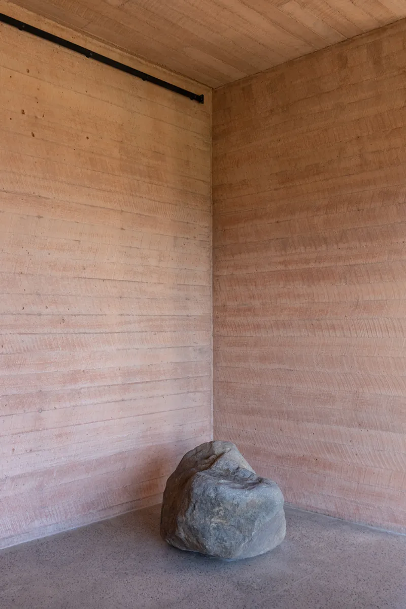 Corner of rammed earth room with single boulder on polished concrete floor