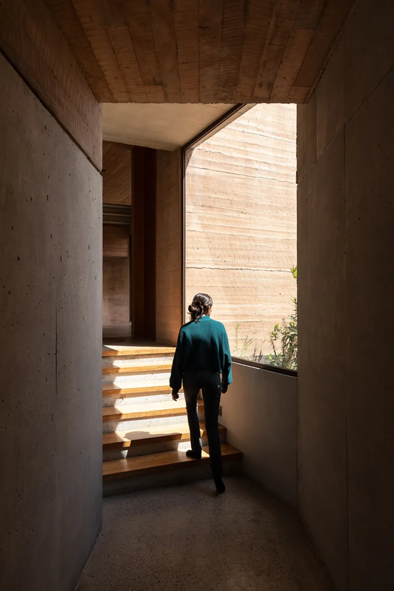 Person ascending timber stairs between concrete walls under a wood-paneled ceiling with afternoon light