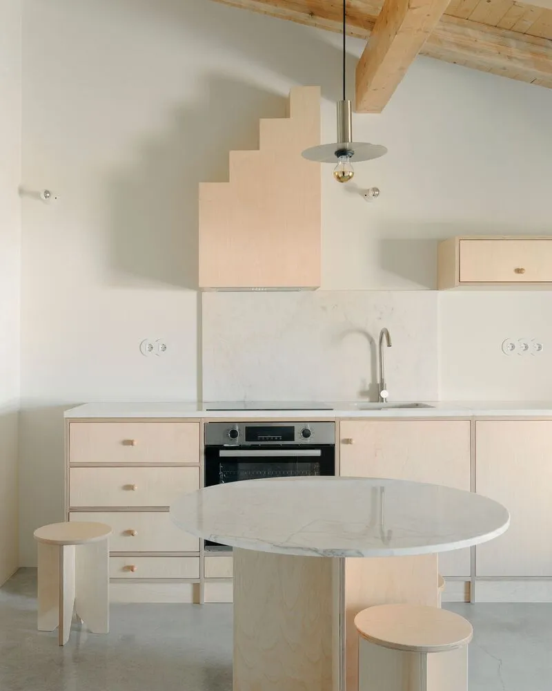 Kitchen with pale plywood cabinetry, marble countertop and pendant light below exposed timber ceiling beams
