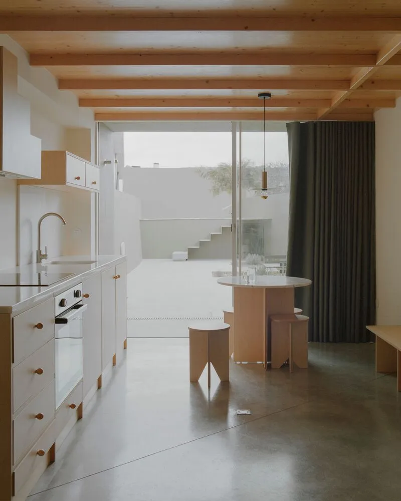 Kitchen and dining area with timber ceiling beams and view to exterior staircase through glazed wall