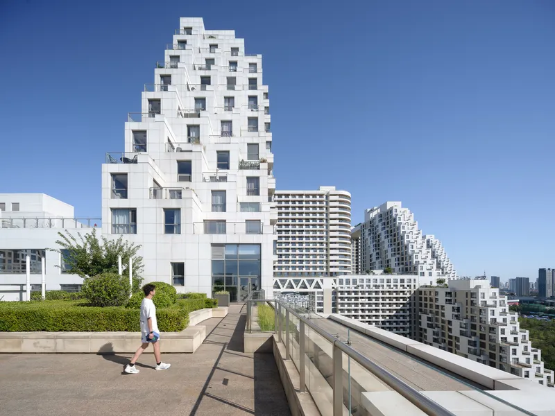 Rooftop terrace with concrete walkway and planted beds overlooking stepped white towers under clear sky