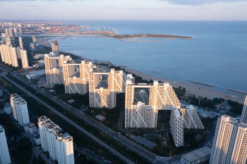 Drone view of residential complex with stepped towers near coastline at golden hour