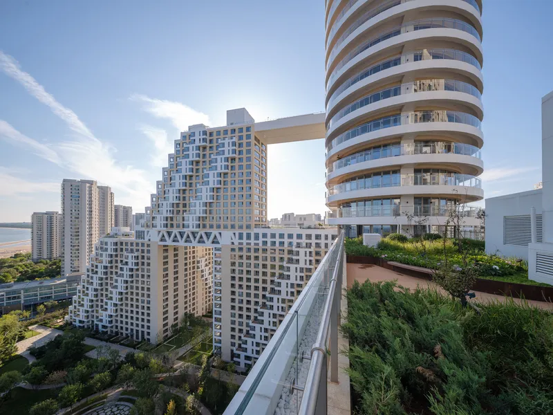 Planted rooftop terrace with grasses and shrubs overlooking neighboring towers connected by sky bridge