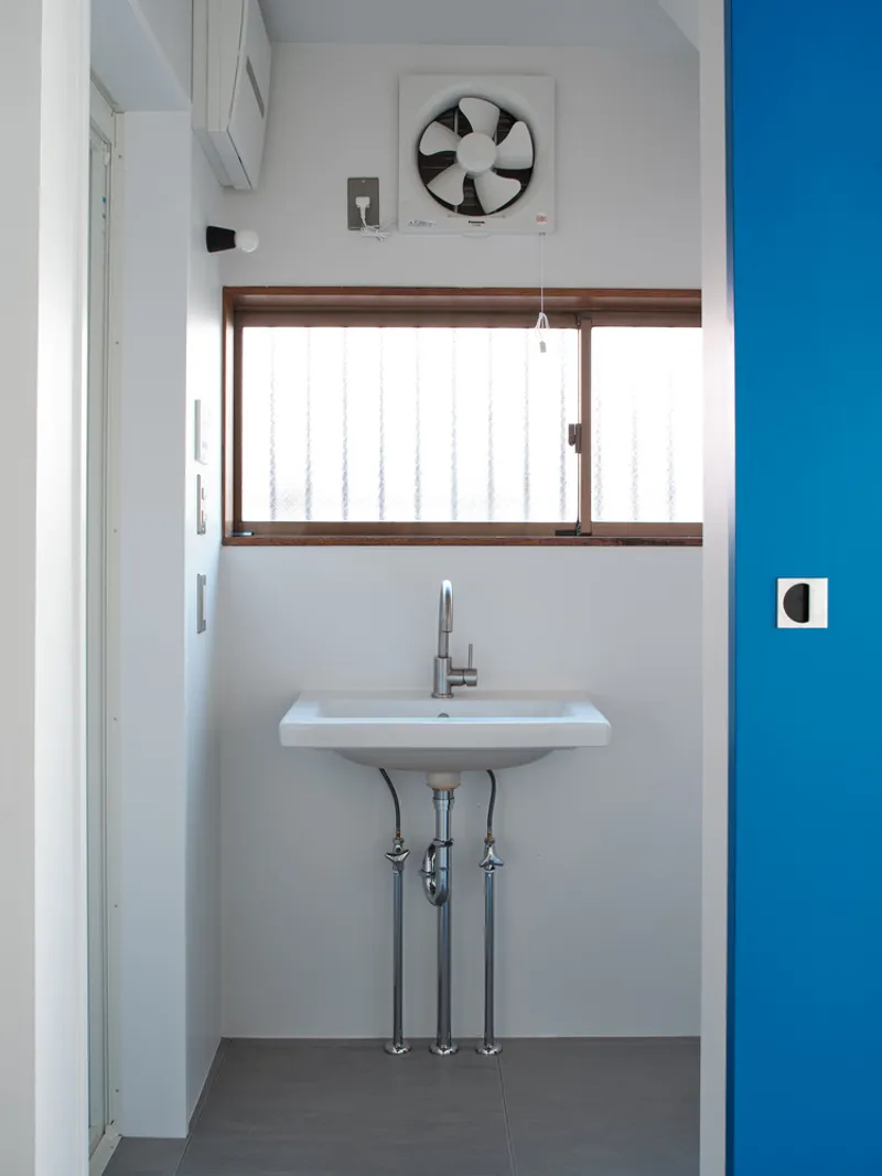 Compact bathroom with wall-mounted sink, exposed plumbing, and timber-framed window below a ceiling ventilation fan