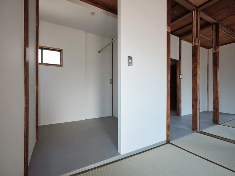 Threshold between tatami mat room and grey-tiled shower area with glass partition and timber columns