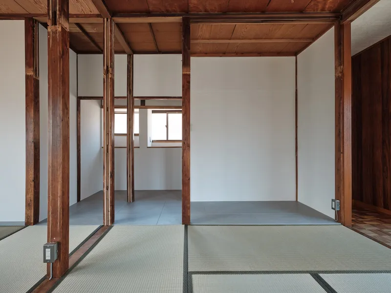 View through timber columns into adjoining tatami rooms with grey tile flooring and exposed beam ceiling