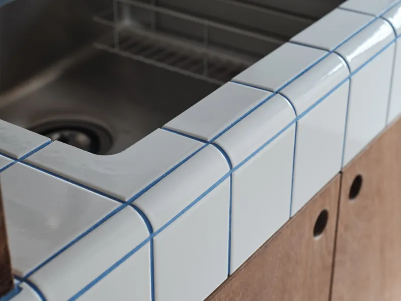 Close-up of the white tiled counter edge with blue grout lines meeting a timber cabinet