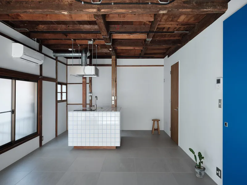Open-plan interior with exposed timber ceiling beams and white-tiled kitchen island on grey floor