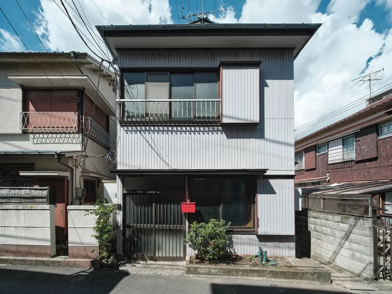 Street facade with corrugated metal cladding and cantilevered balcony under blue sky with power lines
