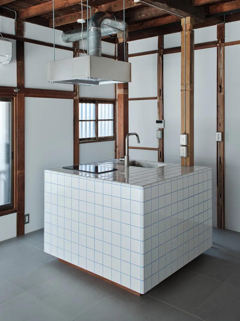 Freestanding kitchen island with white tile cladding and stainless steel countertop under suspended range hood