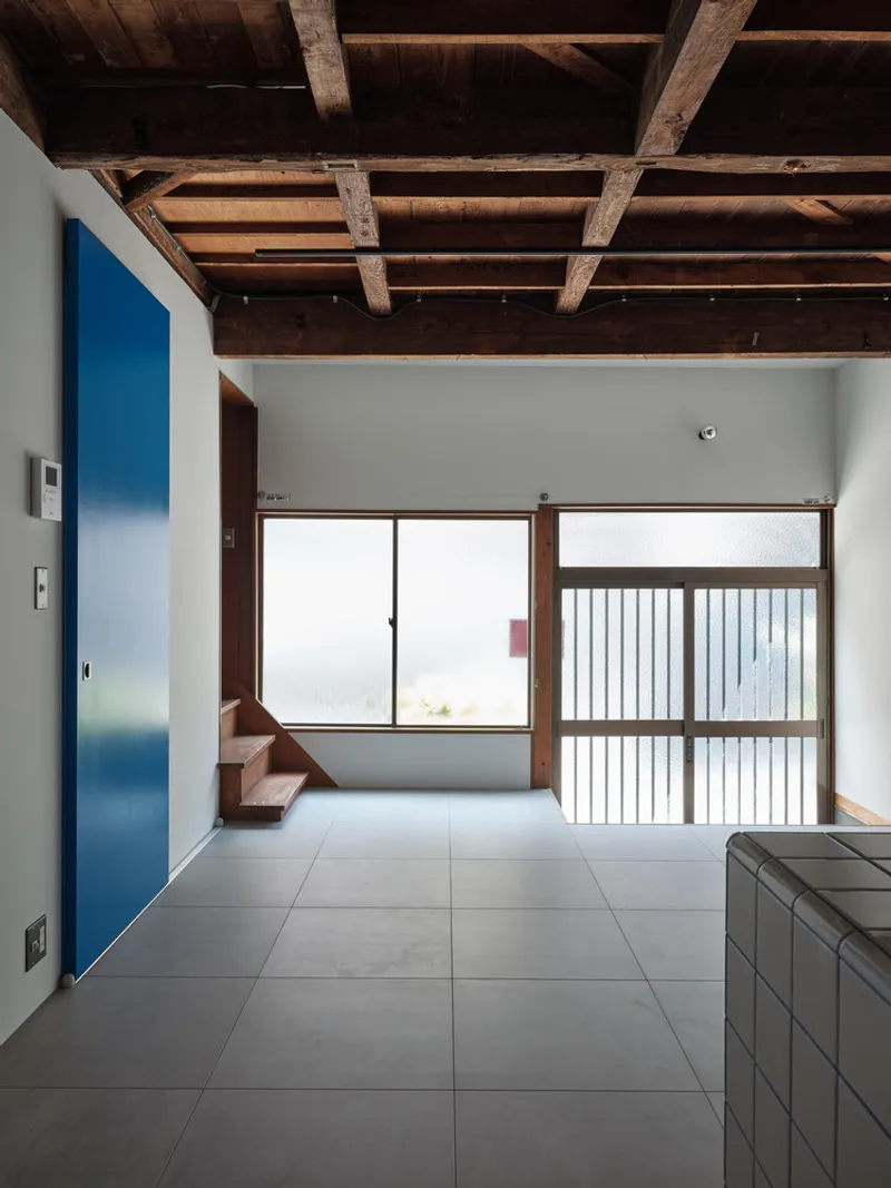 Interior view with exposed timber ceiling beams above grey tile floor and sliding screens with vertical slats