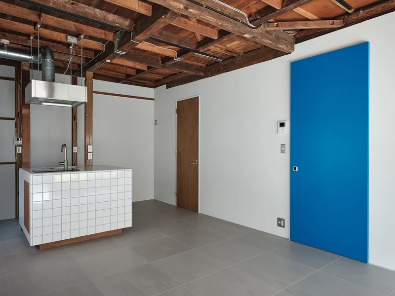 White wall with flush blue door panel beside tiled kitchen counter under weathered timber ceiling