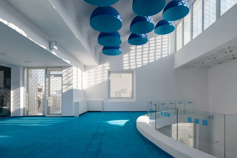 Interior prayer hall with blue floor tiles and turquoise pendant lights beneath geometric white ceiling coffers