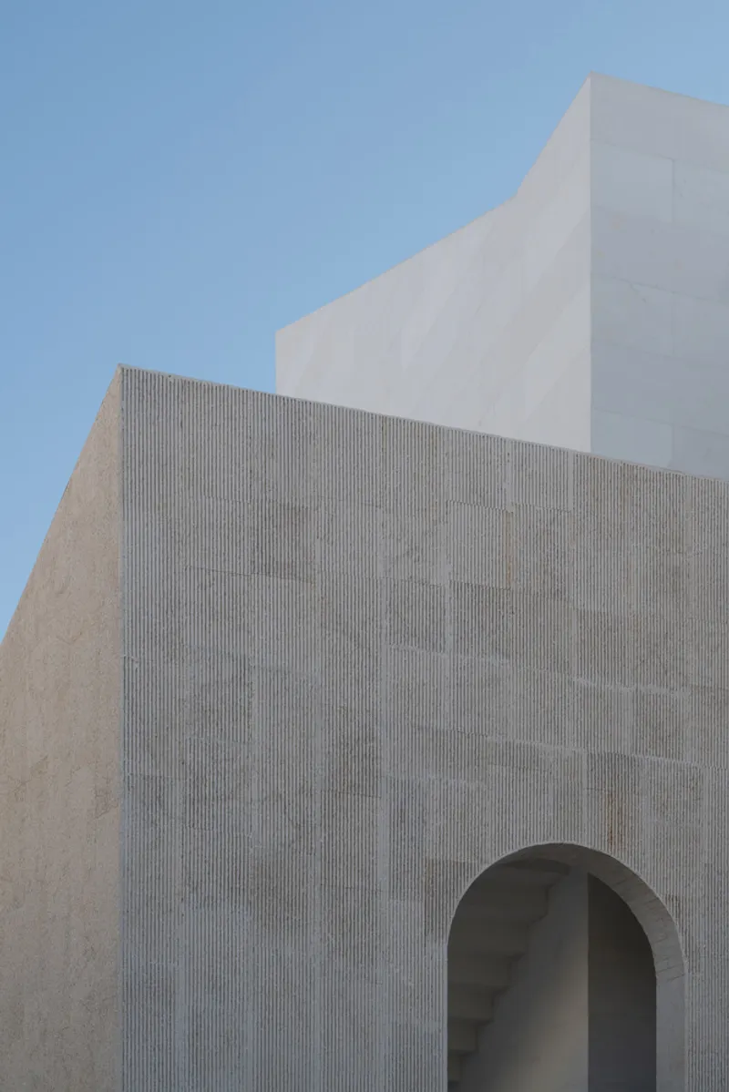 Close-up of the ridged concrete facade with arched opening against a clear sky